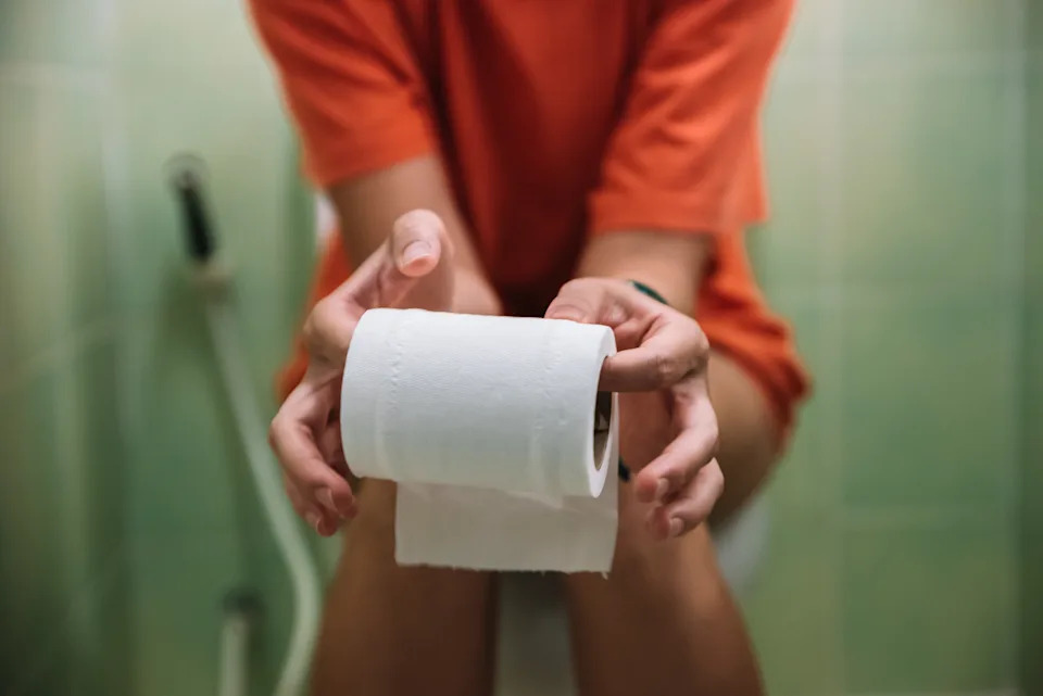 Primer plano borroso de una persona sentada en un inodoro sosteniendo un rollo de papel higiénico
