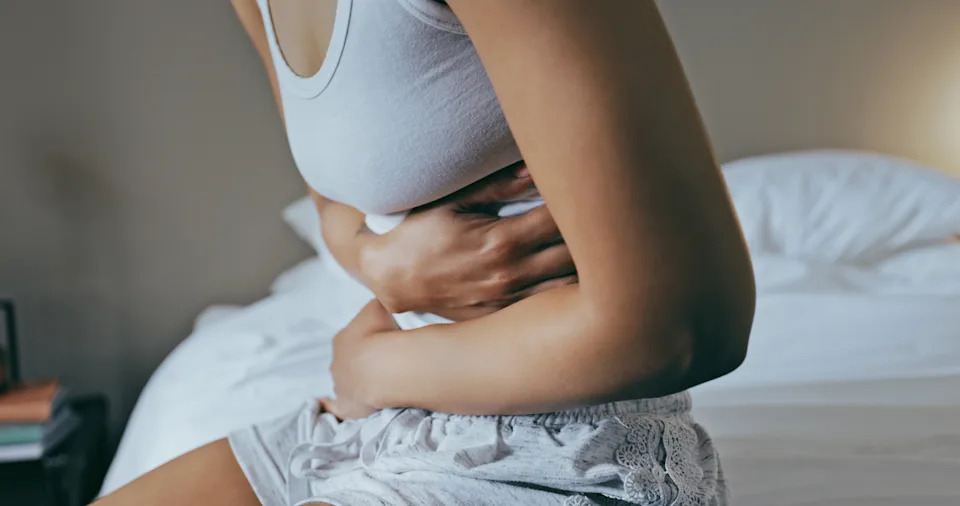 Primer plano de una mujer sentada en el borde de la cama con dolor de estómago