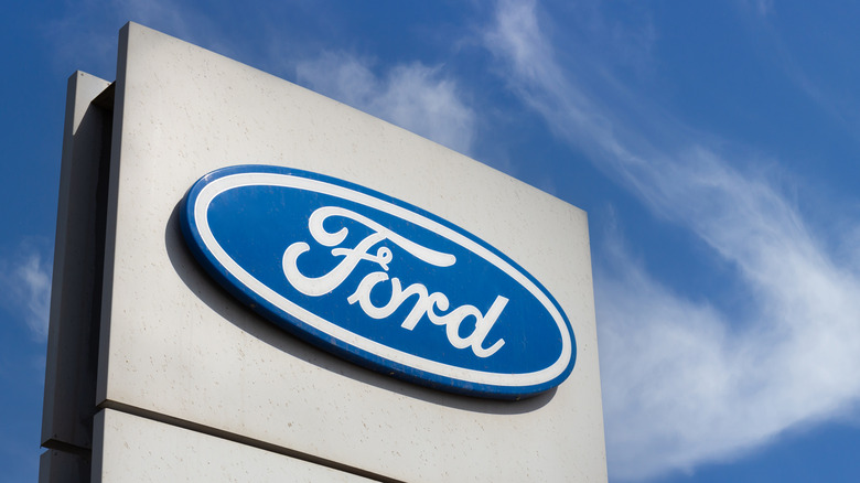 Primer plano del logotipo de la marca Ford sobre fondo de cielo azul. Centro de concesionario de coches