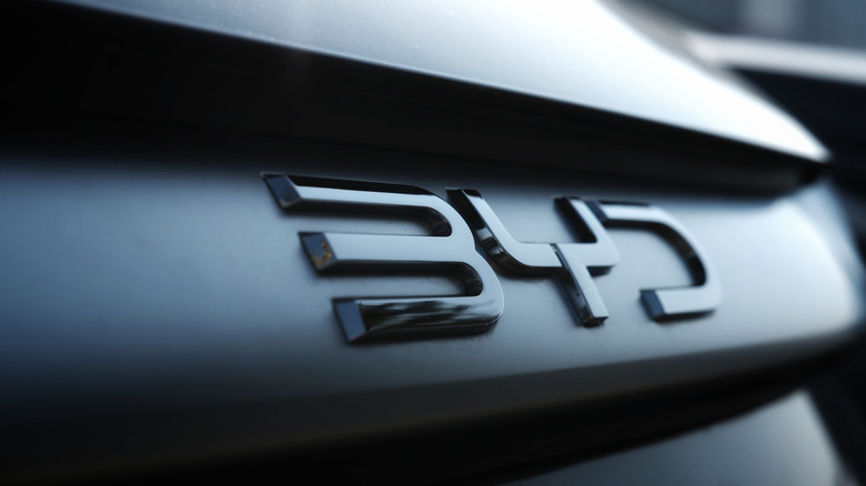 Primer plano de un emblema metálico 'BYD' en la parte trasera oscura de un automóvil moderno, resaltando los elegantes números y detalles automotrices. Foto tomada en Cigombong, Java Occidental, Indonesia, el 7 de junio de 2025.