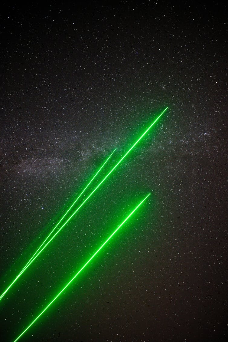 Tres rayos láser verdes con la Vía Láctea de fondo.