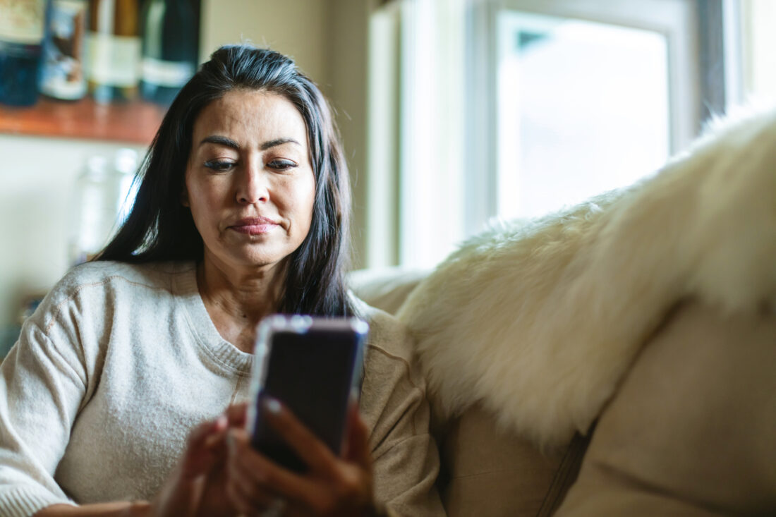Una mujer madura con cabello largo está usando un teléfono inteligente.