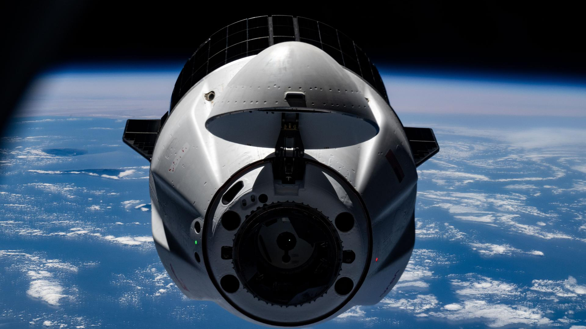 Vista frontal en primer plano de una cápsula espacial blanca cónica con la Tierra al fondo