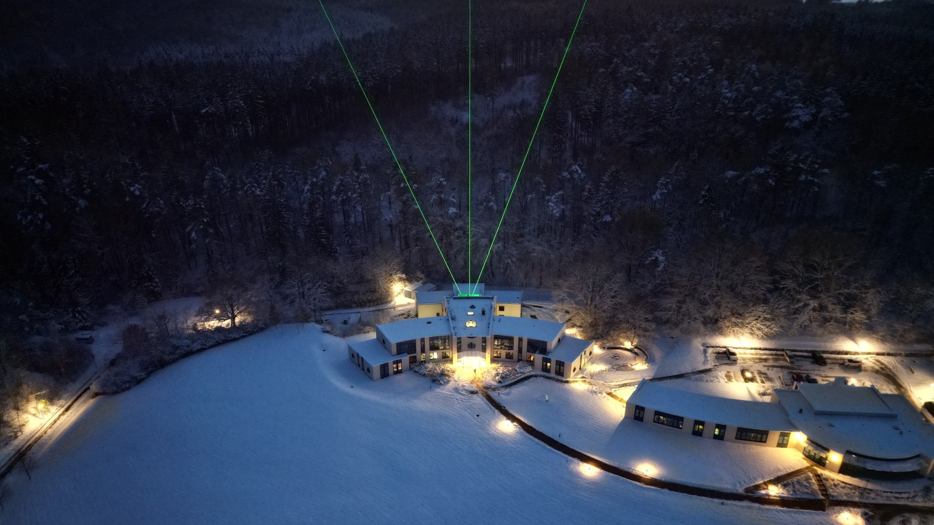 tres rayos de luz verdes se disparan hacia el cielo desde un edificio rodeado por un paisaje alpino nevado