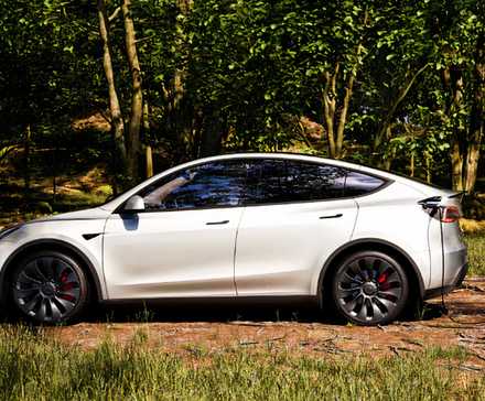 Un pequeño SUV eléctrico Tesla Modelo Y blanco se está cargando al aire libre. 