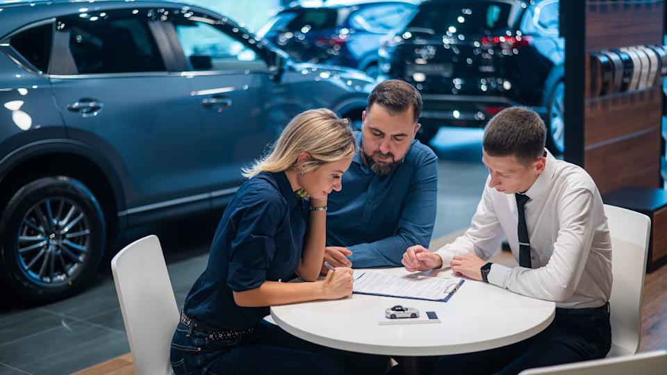Feliz pareja caucásica firmando un contrato para comprar un concesionario de automóviles.